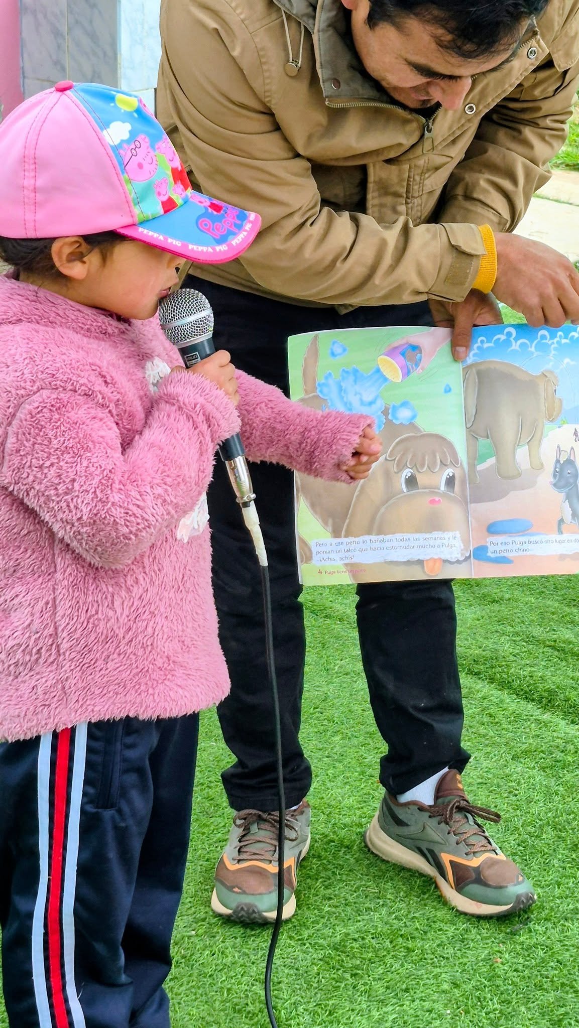 Una niña comparte la historia con el micrófono y el apoyo del docente.